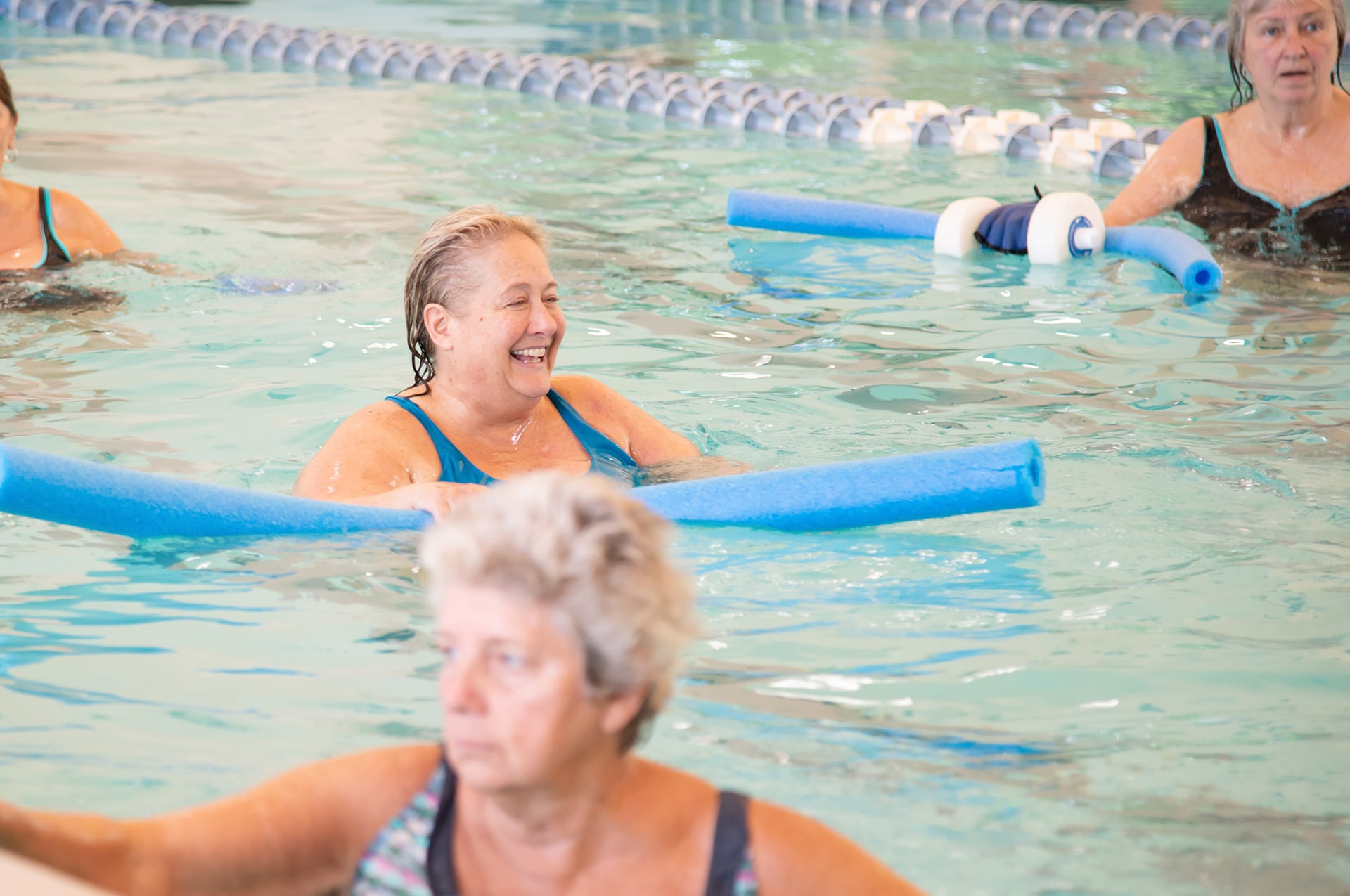 Senior woman laughing in pool with pool noodle