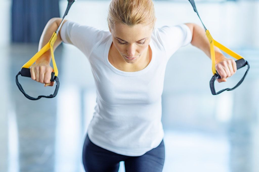 woman with hands in TRX bands doing standing push ups