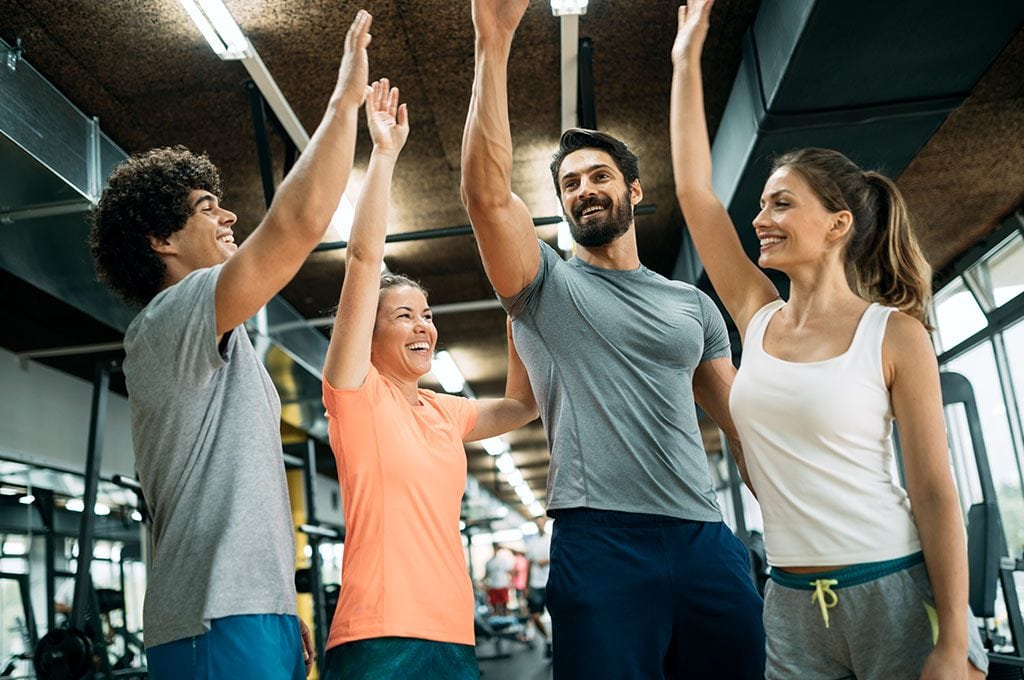 group of fit people high fiving in gym after indoor cycling class