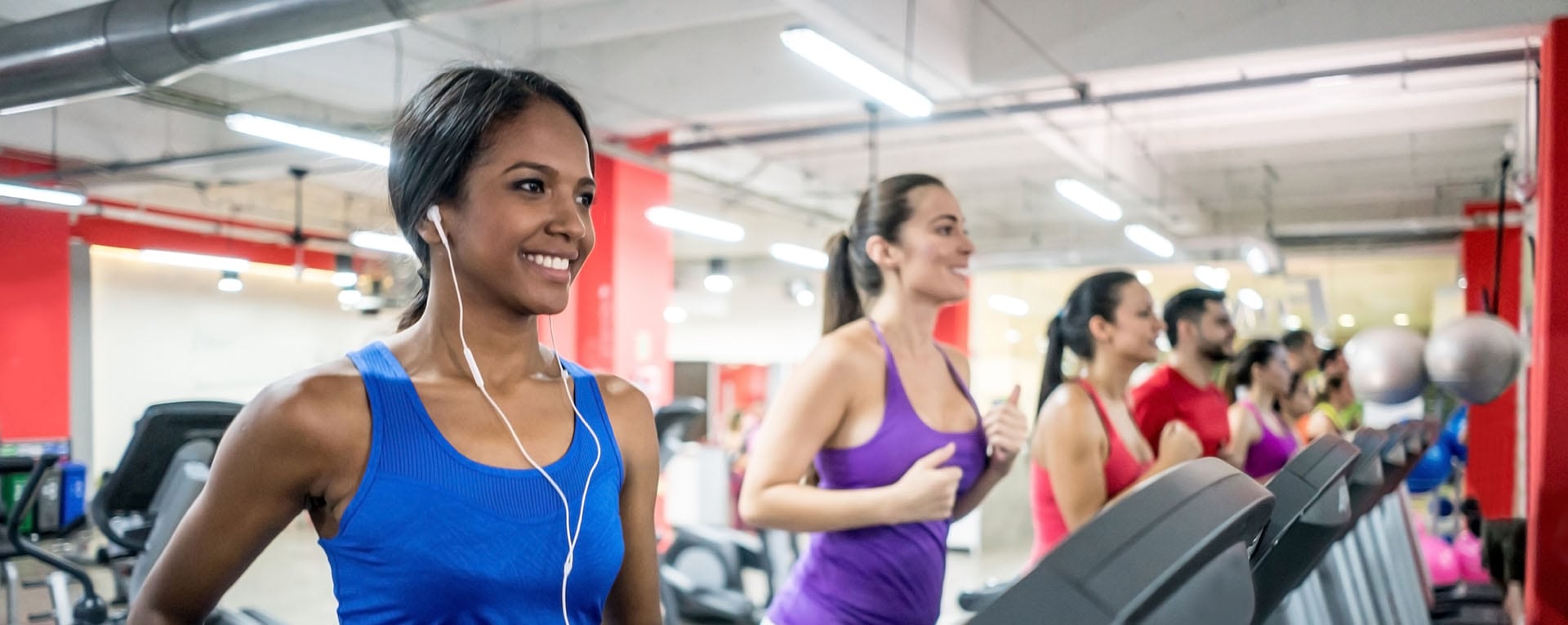 group of bright fit people running on treadmills, listening to music with earbuds