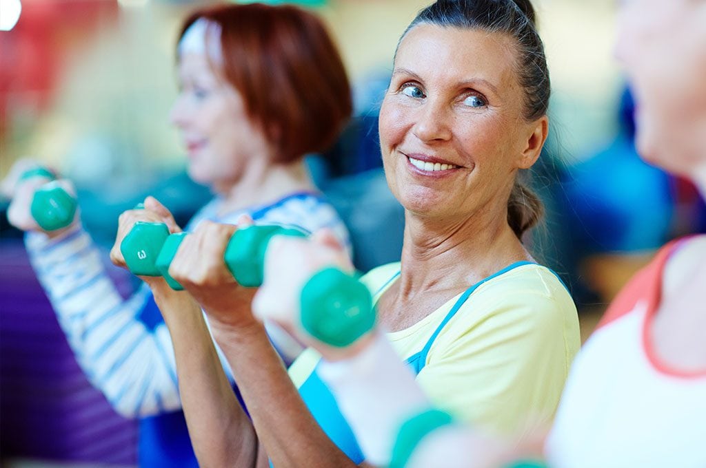 smiling woman lifting 2 pound weights in a fitness group class