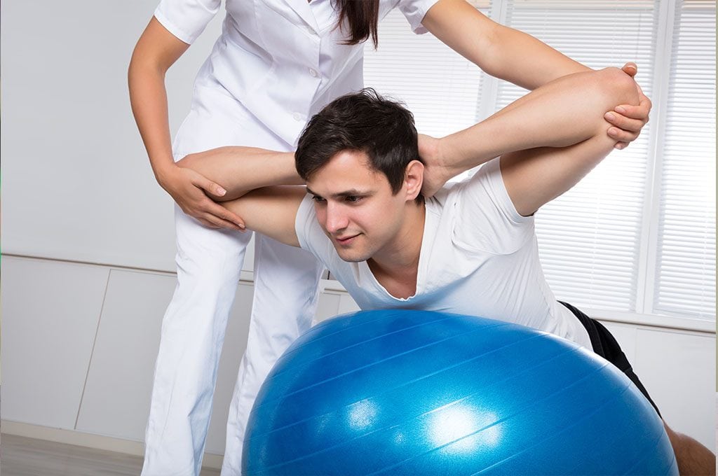 Female physical therapist stretching a man upward on a yoga ball