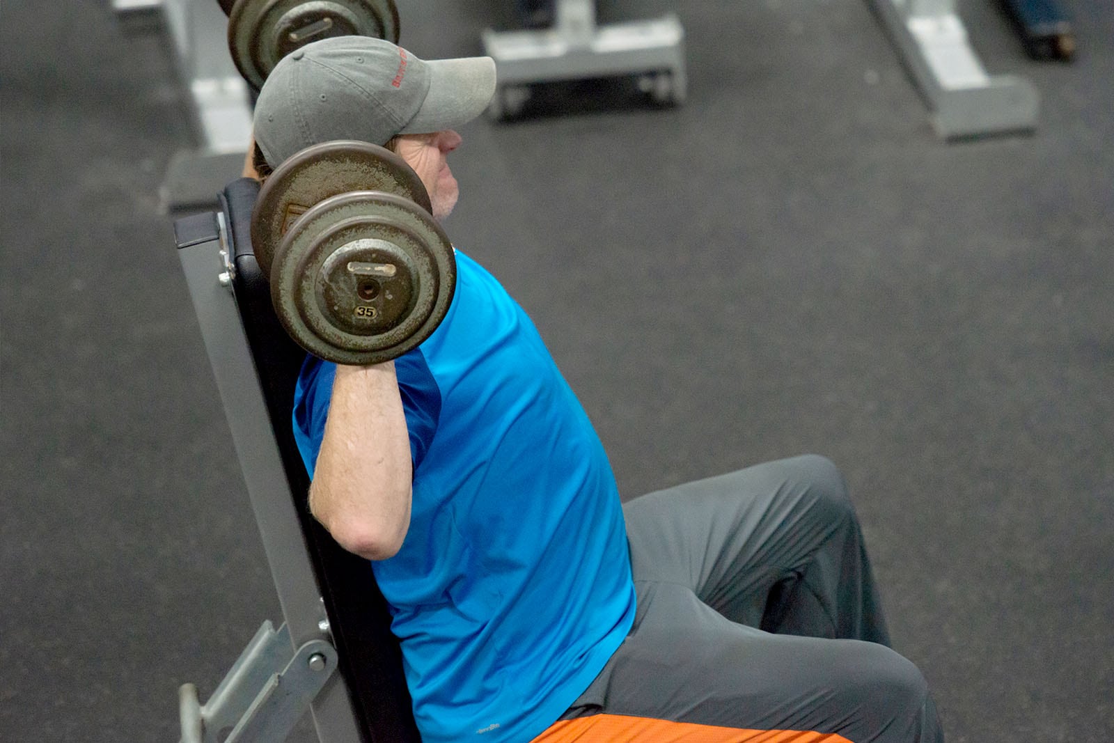 Man in blue shirt lifting weights while sitting