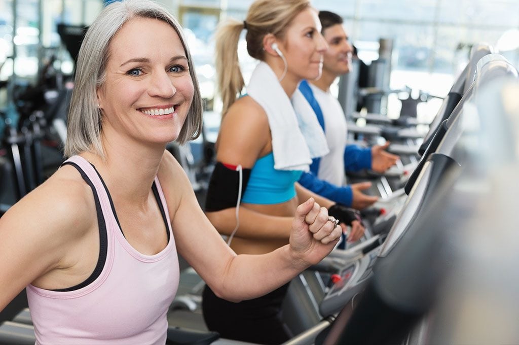 smiling woman on a cardio machine with gym members in background on treadmills