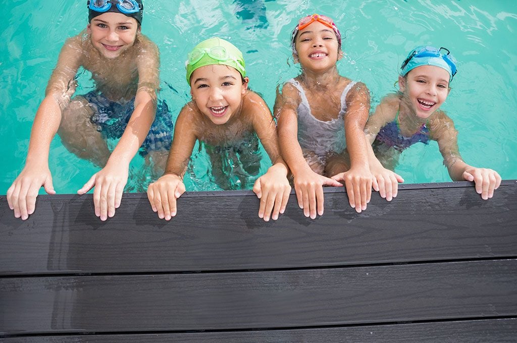 children smiling and holding onto the side of a pool