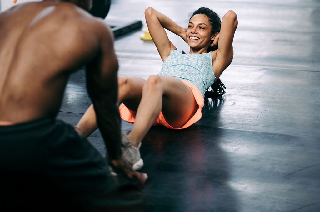 male personal trainer holding a woman's ankles while she does sit ups