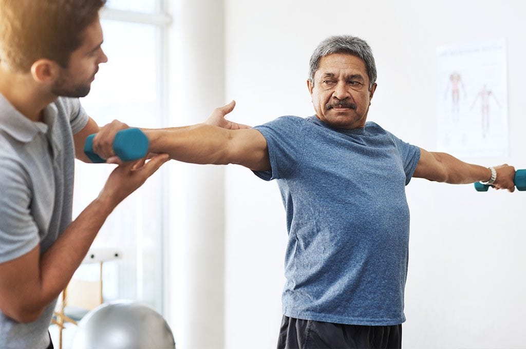 male personal trainer explaining to an older gentleman how to properly use his dumbbells for best results