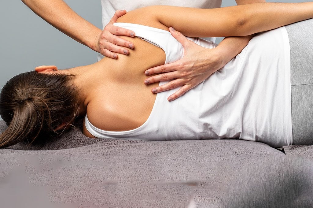 woman on her side, while a physical therapist is adjusting her shoulder blade