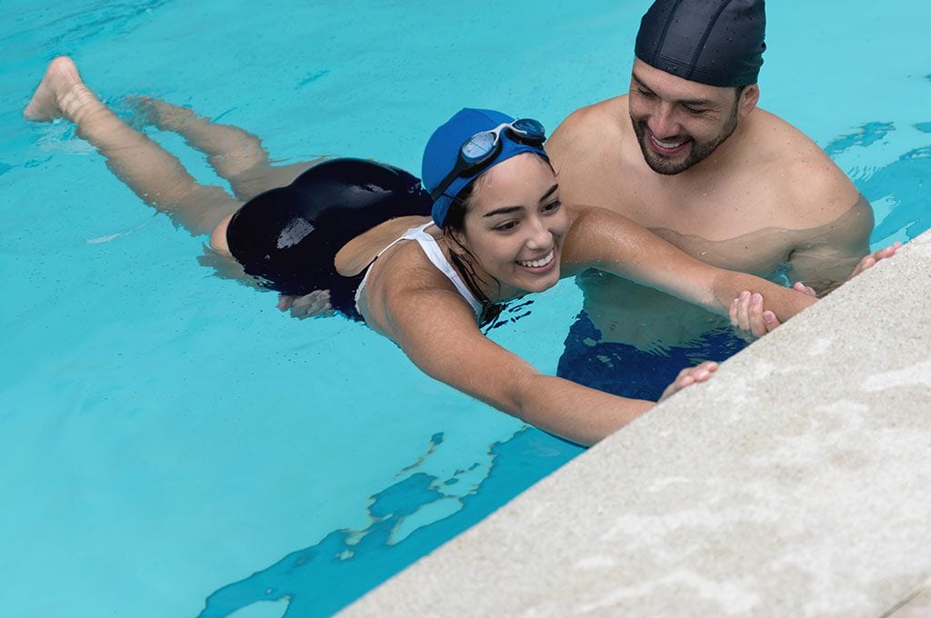 male instructor teaching a femal swim student to kick while holding side of pool