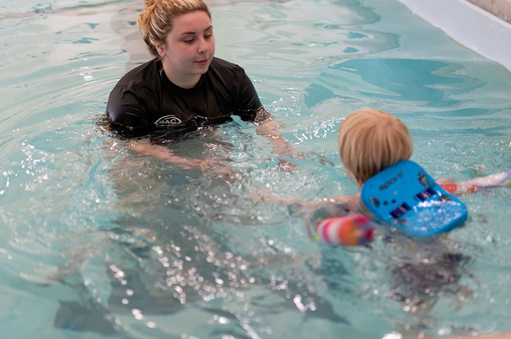 female swim teacher helping a boy swim with a life jacket on