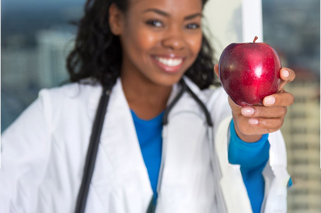woman doctor holding up an apple and smiling