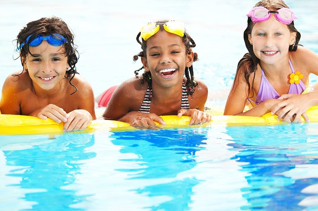 3 kids in pool, smiling. floating on a yellow raft