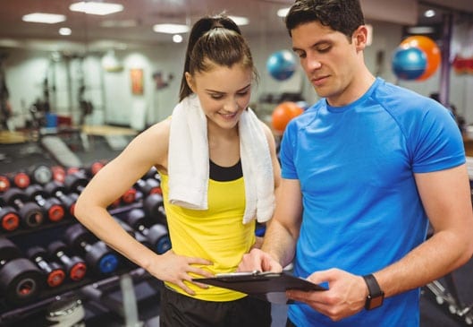 woman after workout reviewing progress chart with personal trainer at gym