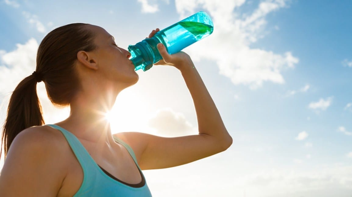woman drinking water outside with sun reflecting on neck