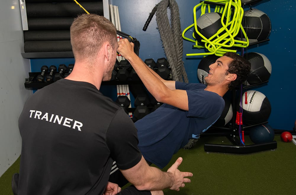 man using functional training equipment at gym as trainer provides support