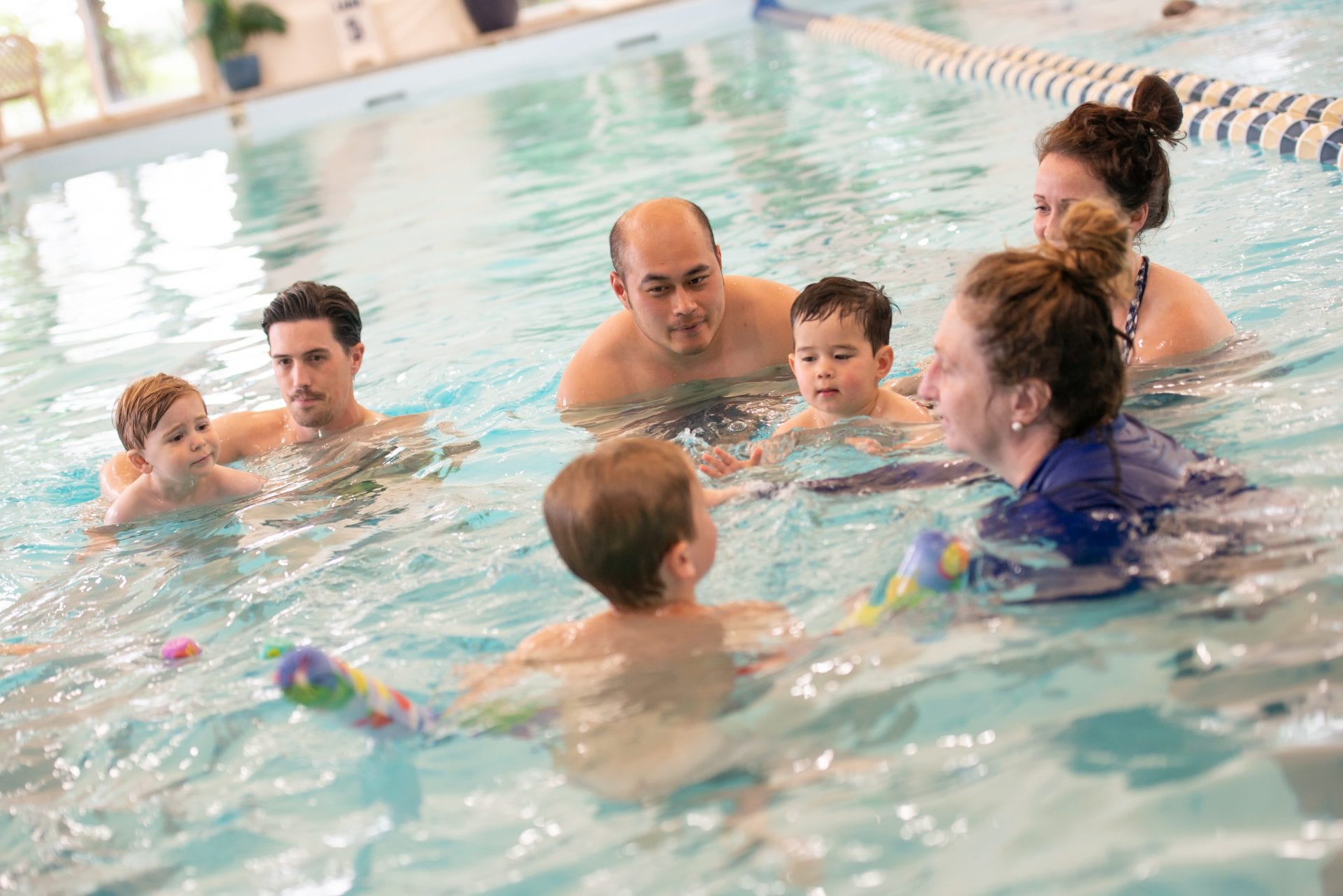 families in pool with swim instructor for swim lessons