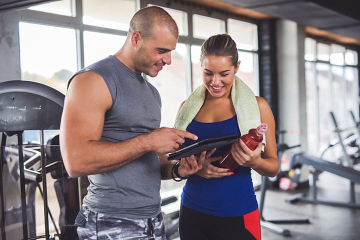 Young Woman Discussing Workout Progress With Fitness Instructor at gym